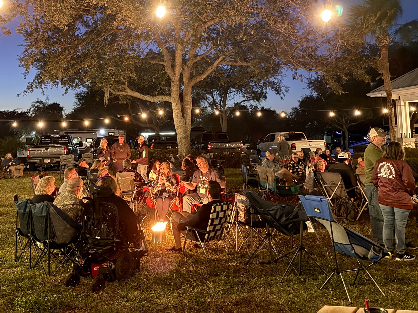Attendees gathered around a campfire under string lights at the Tampa Campout
